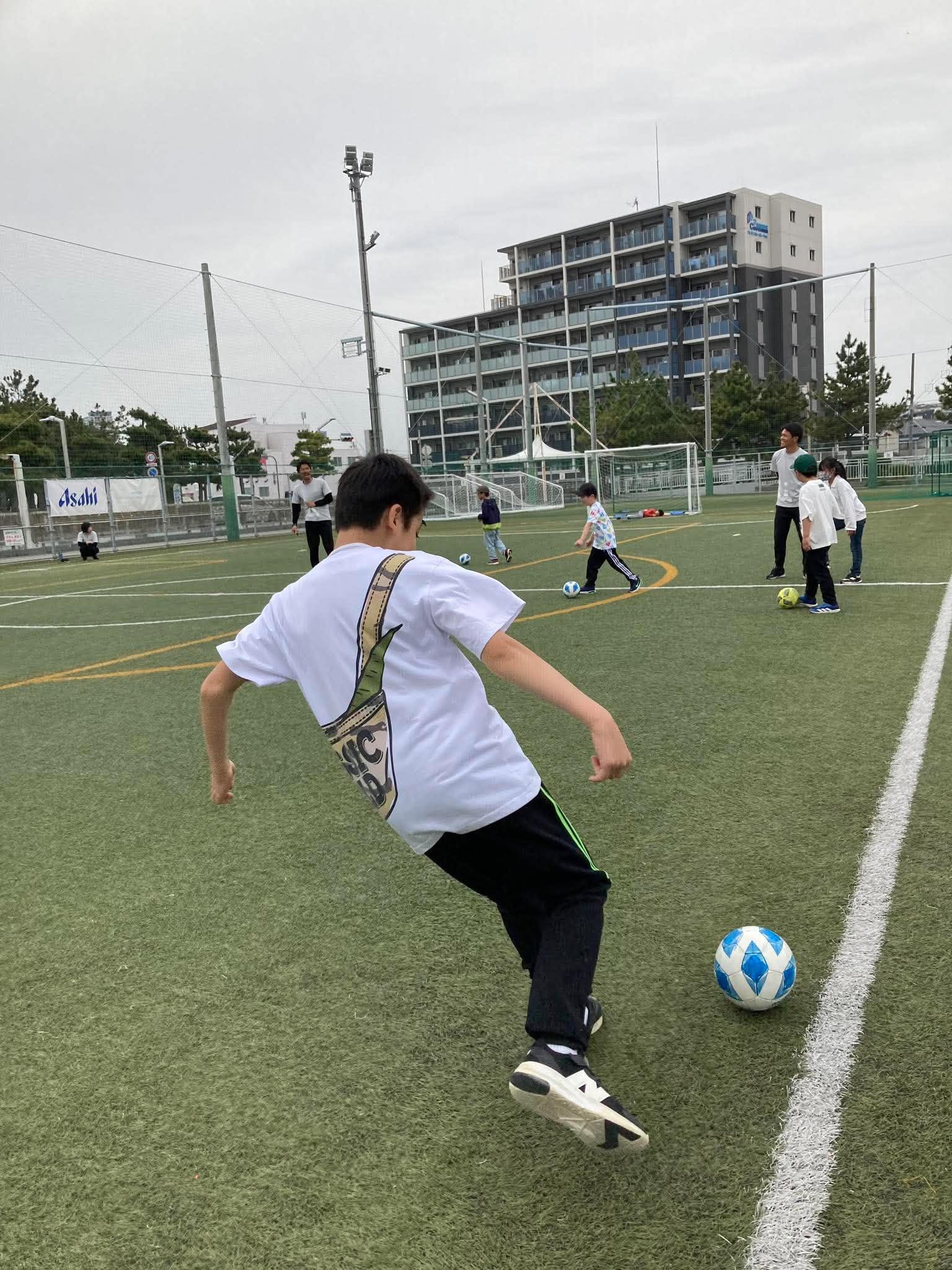 ボールを蹴る子どもと見守るコーチ